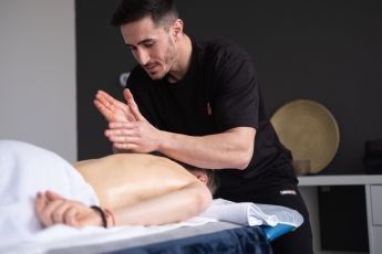 Crop anonymous medical specialist rubbing shoulders of male client lying on couch in medical salon